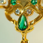 Close-up of the Deep Green Jadeite Drop Earring, a Chinese-inspired design in gold-plated 925 sterling silver, featuring an ornate filigree with a large teardrop jadeite stone and smaller round green and clear gemstones.