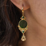 A close-up of a person’s ear wearing the Deep Green Jadeite Drop Earring—Chinese-inspired filigree in gold-plated 925 sterling silver, with a circular jade centerpiece and teardrop accents.