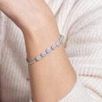 A person in a cream ribbed sweater showcases the Greenish White Jadeite Halo Tennis Bracelet, featuring large, round, sparkling gemstones on their wrist.