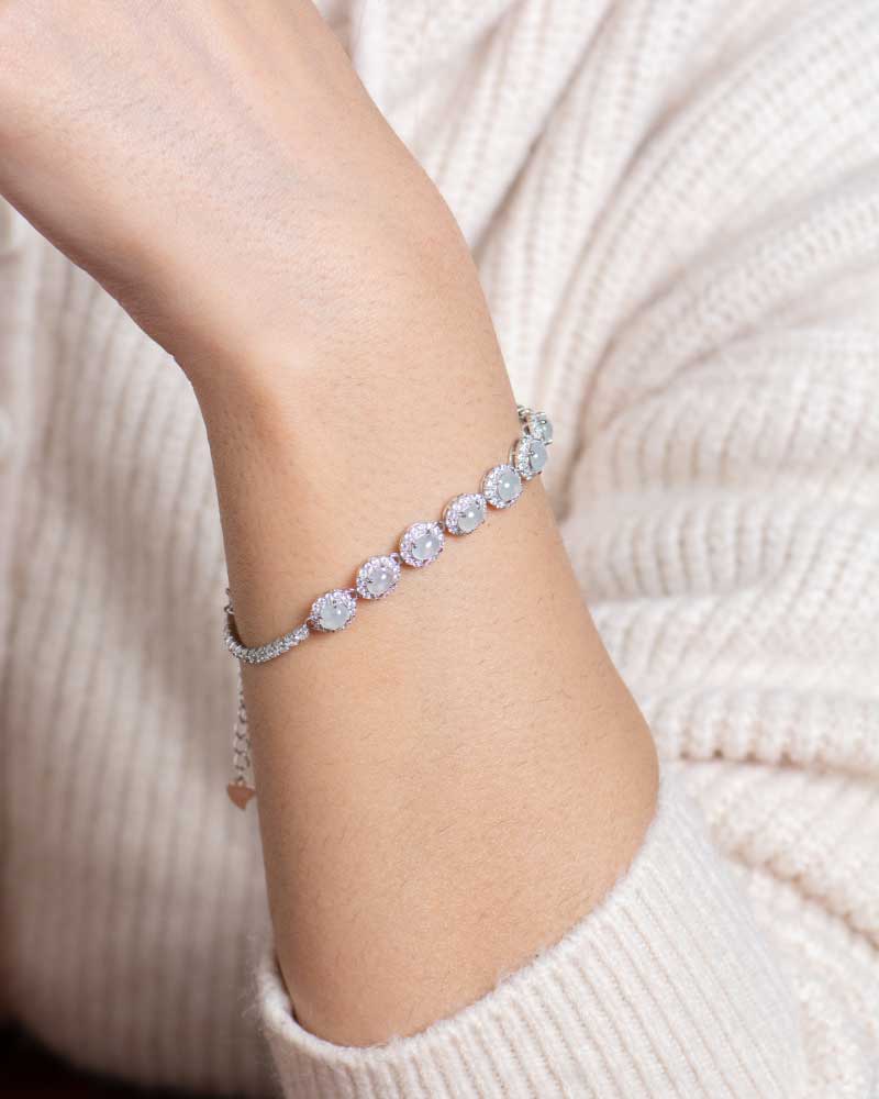LYU_5163 A person in a cream ribbed sweater showcases the Greenish White Jadeite Halo Tennis Bracelet, featuring large, round, sparkling gemstones on their wrist.