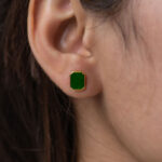 Close-up of a person’s ear with brown hair tucked behind it, wearing a Vivid Green Jadeite Stud Earring – a rectangular flat inlay set in gold-plated 925 sterling silver.