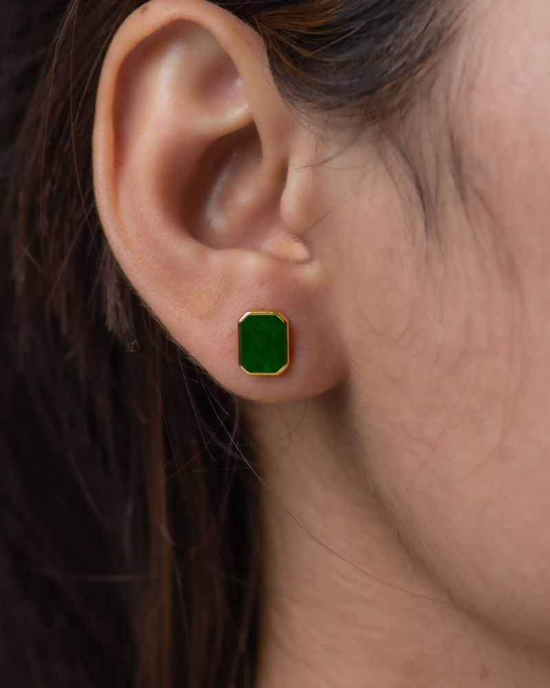 Close-up of a person’s ear with brown hair tucked behind it, wearing a Vivid Green Jadeite Stud Earring – a rectangular flat inlay set in gold-plated 925 sterling silver.
