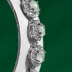Close-up of the Greenish White Jadeite Halo Tennis Bracelet, featuring round greenish white jadeite gems encircled by clear crystals, displayed on a green background.