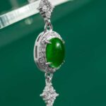 A close-up of the Vivid Green Jadeite Halo Link Bracelet, showcasing central oval domed cabochons in high-polish sterling silver with clear stone accents, set against a green background.