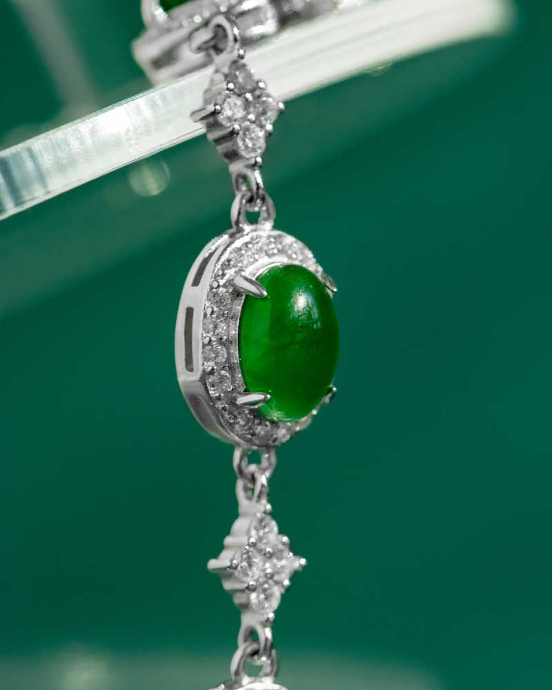 LYU_5288 A close-up of the Vivid Green Jadeite Halo Link Bracelet, showcasing central oval domed cabochons in high-polish sterling silver with clear stone accents, set against a green background.