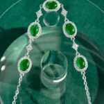 The Vivid Green Jadeite Halo Link Bracelet features domed green cabochons in high-polish sterling silver, arranged symmetrically and displayed on a round glass stand over a green background.