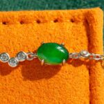 A close-up of the Vivid Green Jadeite Link Bracelet, showcasing its oval cabochons set in high-polish sterling silver, displayed on an orange textured surface.