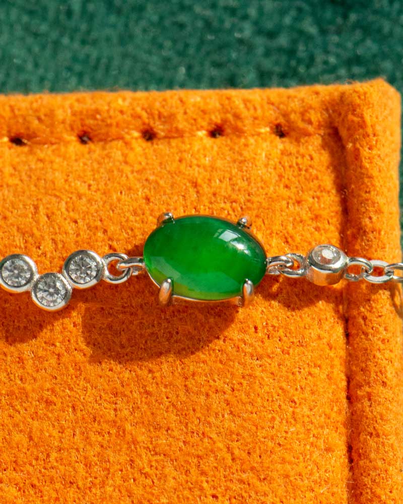 A close-up of the Vivid Green Jadeite Link Bracelet, showcasing its oval cabochons set in high-polish sterling silver, displayed on an orange textured surface.