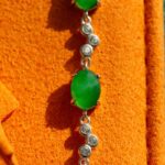 A vivid green jadeite link bracelet featuring oval cabochons in high-polish sterling silver, displayed on an orange textured surface.