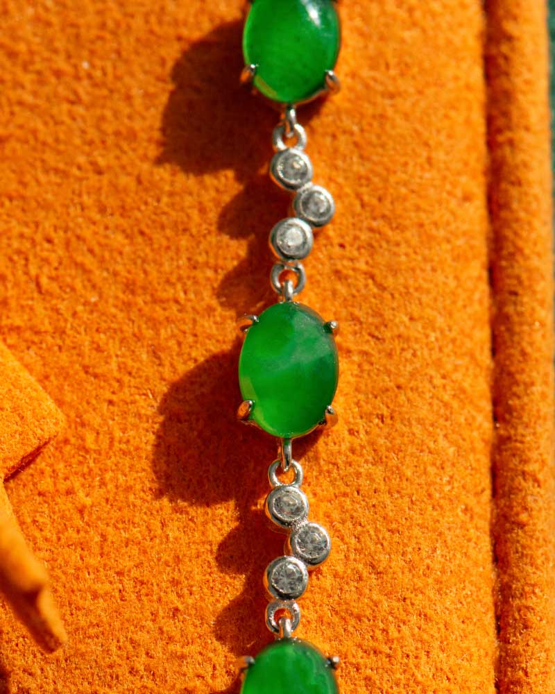 A vivid green jadeite link bracelet featuring oval cabochons in high-polish sterling silver, displayed on an orange textured surface.