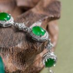 A close-up of the Vivid Green Jadeite Halo Link Bracelet, featuring domed cabochons set in high-polish sterling silver, displayed on a textured wooden surface.