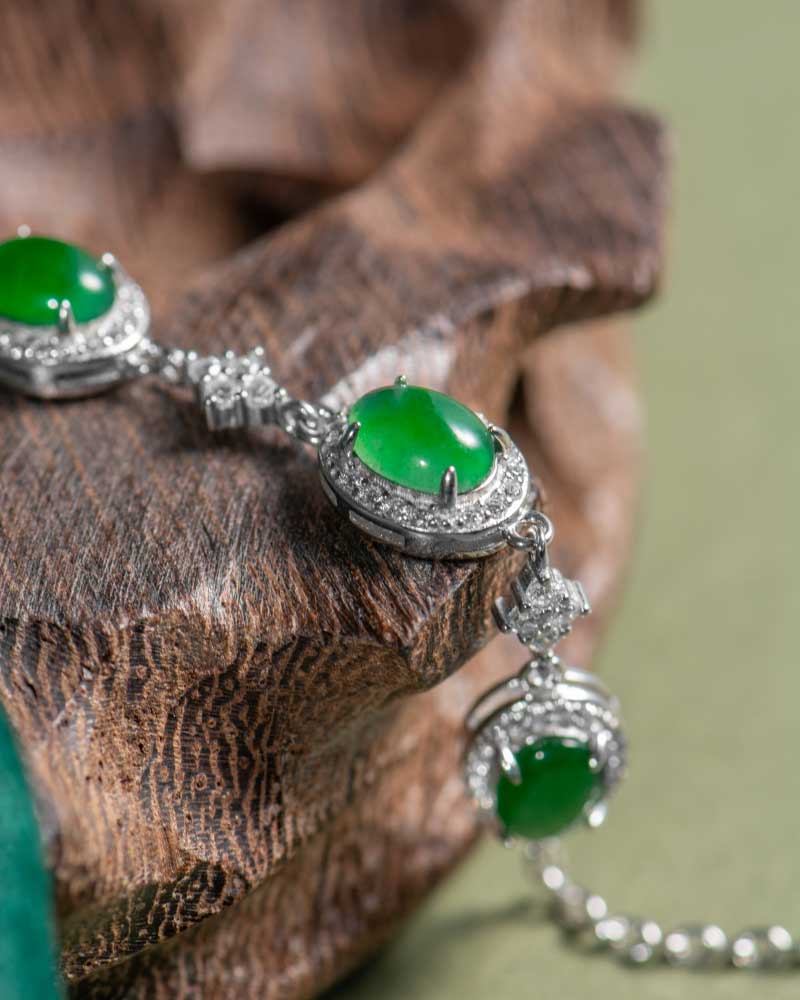LYU_5304 A close-up of the Vivid Green Jadeite Halo Link Bracelet, featuring domed cabochons set in high-polish sterling silver, displayed on a textured wooden surface.