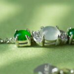 Close-up of the Green & Greenish White Jadeite Halo Station Bracelet—oval cabochons set in high-polish sterling silver—featuring green and translucent gemstones, on a light green surface with a softly blurred chain and clasp.