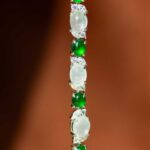 A close-up of the Green & Greenish White Jadeite Halo Station Bracelet, showcasing alternating oval cabochons set in high-polish sterling silver, against a blurred brown background.