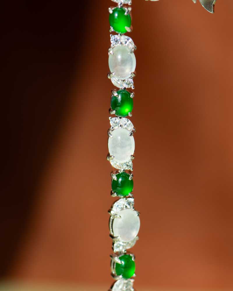 LYU_5330 A close-up of the Green & Greenish White Jadeite Halo Station Bracelet, showcasing alternating oval cabochons set in high-polish sterling silver, against a blurred brown background.