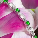 The Greenish White Jadeite Halo Station Bracelet is displayed on pink and white flower petals.