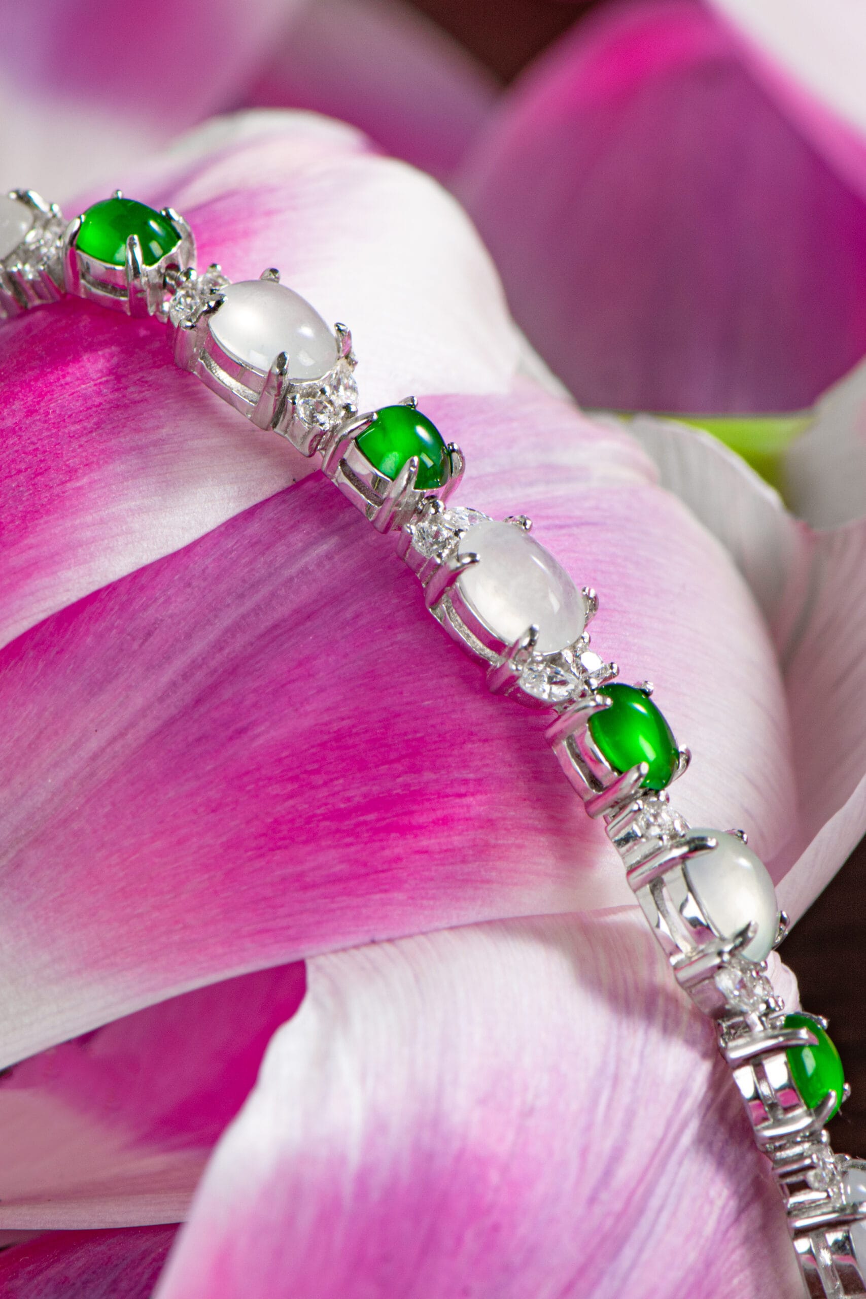 The Greenish White Jadeite Halo Station Bracelet is displayed on pink and white flower petals.