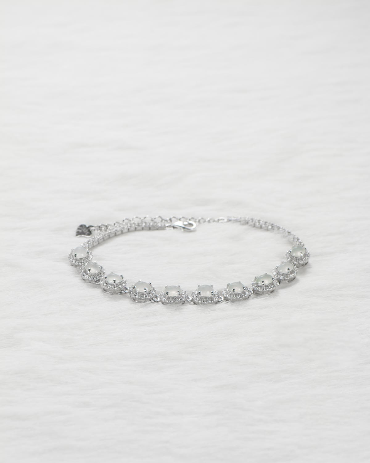 A silver bracelet with large, round, clear gemstones set in a single row, displayed on a soft white textured surface.