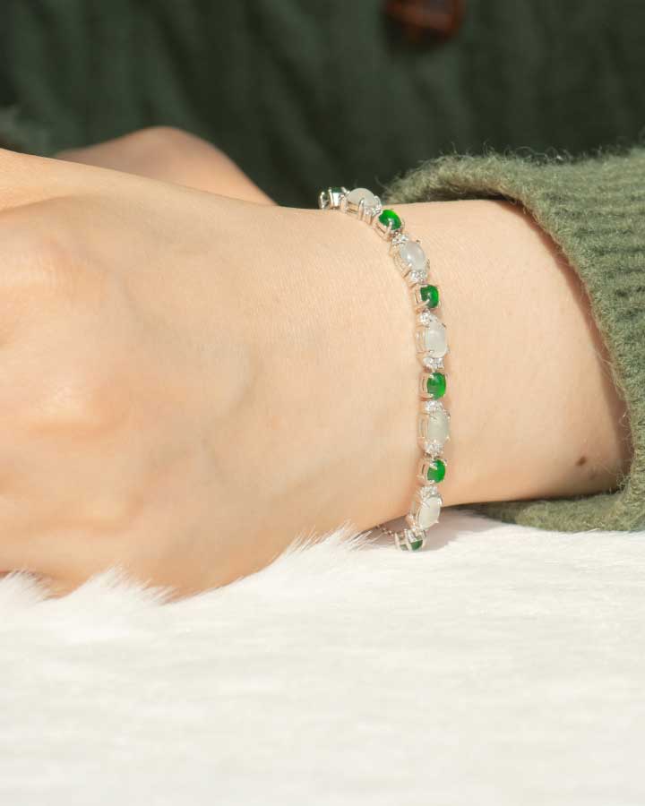 A close-up of a persons wrist wearing a delicate bracelet with alternating green and clear beads. The person is dressed in a green, fuzzy long-sleeve top.