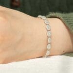 A close-up of a wrist wearing a delicate silver bracelet with oval-shaped, translucent gemstones, against a background of a green sweater and a white surface.