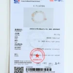 A gemstone testing certificate featuring a photo of a beaded bracelet. The document includes text details on composition, weight (23.115g), color, shape, and a red official stamp. The certificate is predominantly white with blue accents.