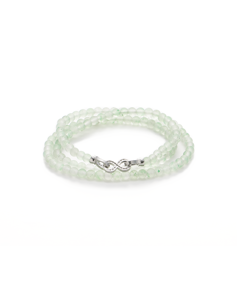 A delicate bracelet made of translucent, pale green beads with a silver infinity symbol clasp, coiled neatly on a white background.