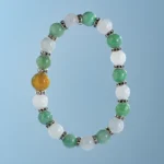 A beaded bracelet with alternating green and white round beads, separated by small silver spacers, and one distinctive yellow bead, displayed against a light blue background.