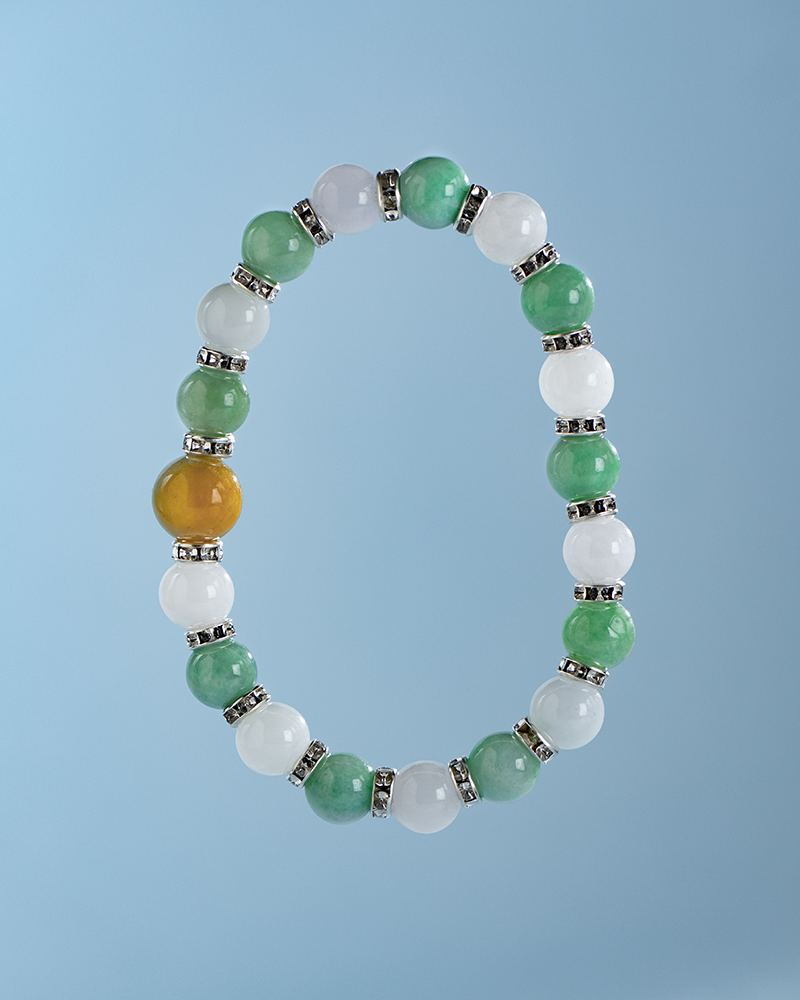 A beaded bracelet with alternating green and white round beads, separated by small silver spacers, and one distinctive yellow bead, displayed against a light blue background.
