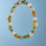 A beaded bracelet with round multicolored stones separated by gold and rhinestone spacers, displayed against a light blue background.