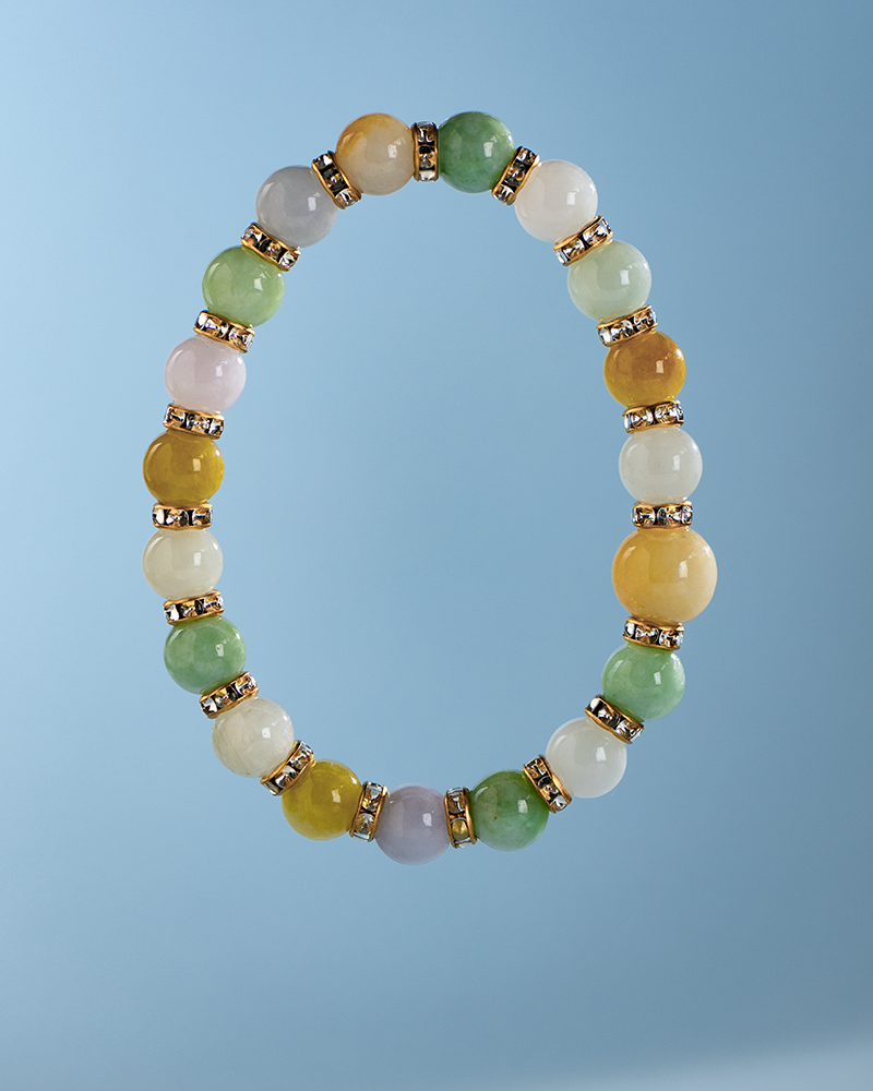 A beaded bracelet with round multicolored stones separated by gold and rhinestone spacers, displayed against a light blue background.