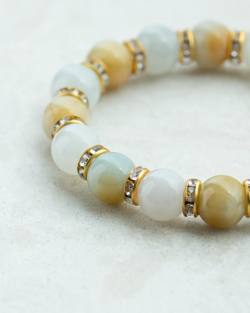 A close-up of the Greenish White and Brownish Yellow Jadeite Bracelet, showcasing spherical jadeite beads in hues of greenish white and brownish yellow, accented with faceted gold and rhinestone spacers on a light textured surface—an elegant example of jadeite jewelry.