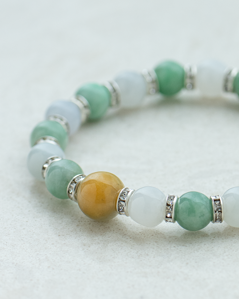 A beaded bracelet with green, white, and one prominent yellow bead, separated by silver spacers, displayed on a light textured surface.