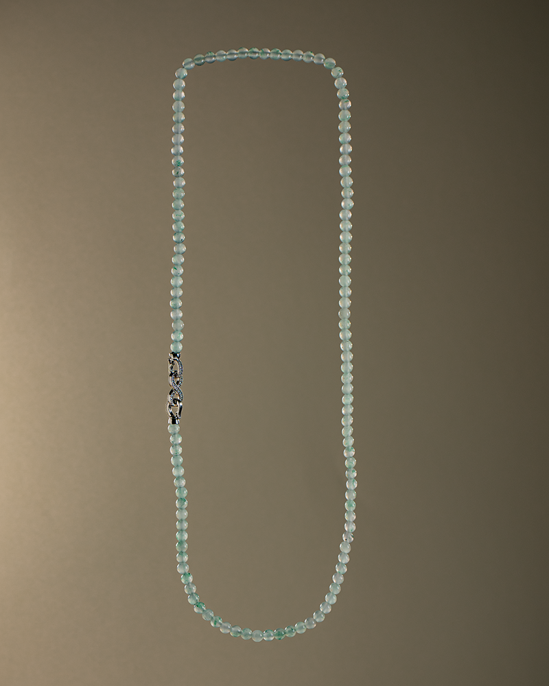 A long necklace made of small, light blue beads with a decorative silver clasp, displayed against a plain brown gradient background.
