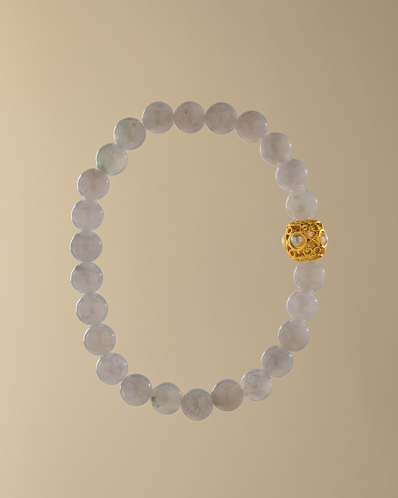 A beaded bracelet made of light gray stones with a single ornate gold bead, displayed on a plain beige background.
