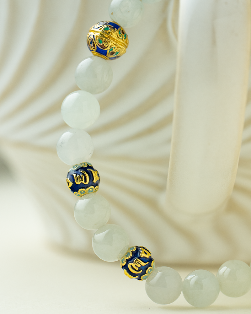A close-up of the Light Green Jadeite Bead Bracelet—spherical beads with warm accents—displayed on the handle of a textured white ceramic cup.