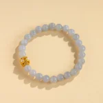 A beaded bracelet made of light gray stones with one gold decorative bead, displayed on a beige background.