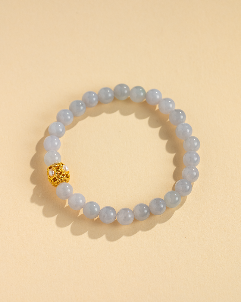 A beaded bracelet made of light gray stones with one gold decorative bead, displayed on a beige background.