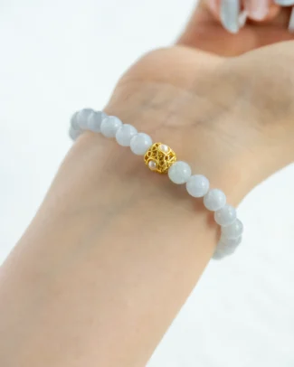 A hand wearing the Greenish-White Jadeite Bead Bracelet, featuring spherical greenish-white beads and a warm-tone accent bead at the center.