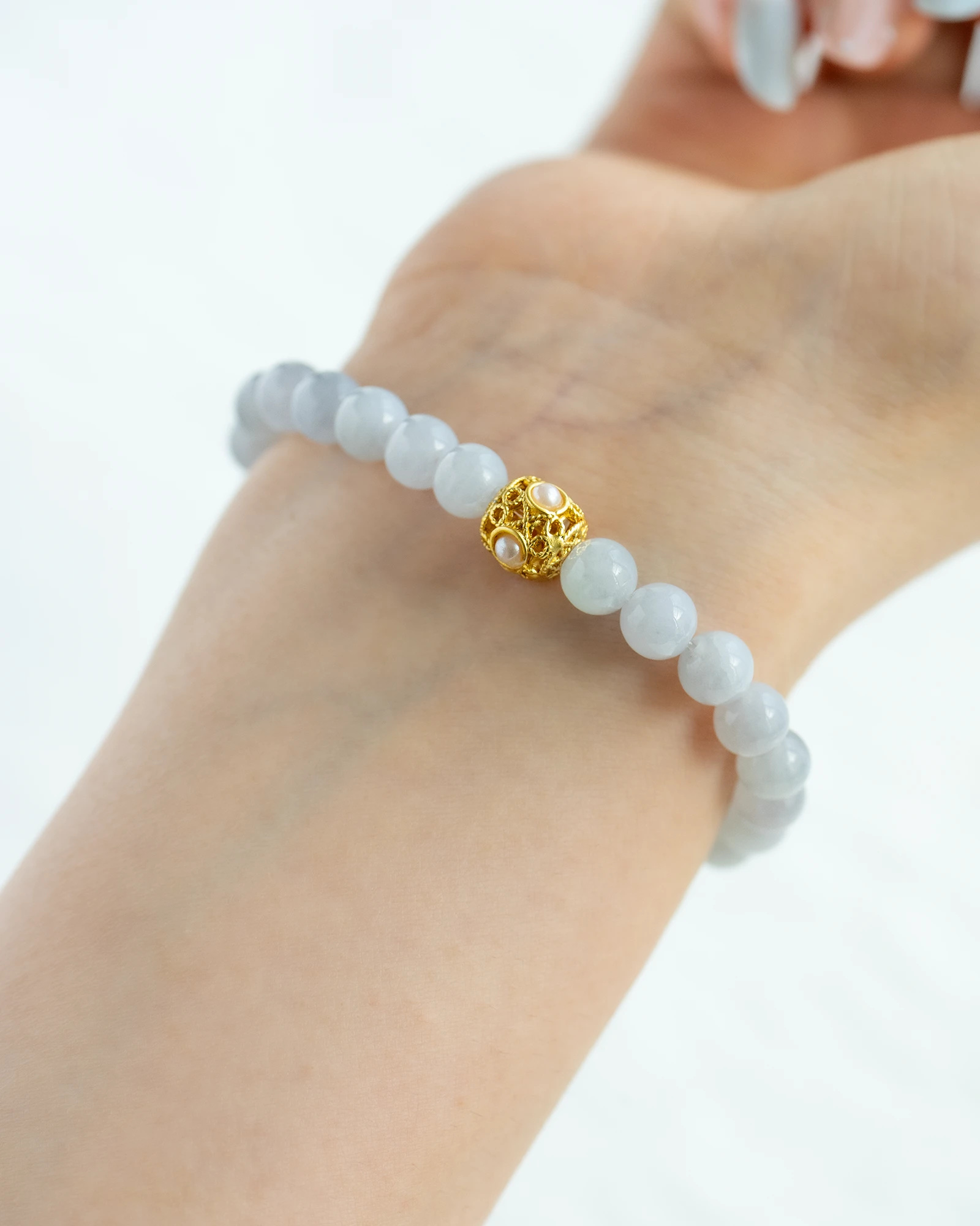 A hand wearing the Greenish-White Jadeite Bead Bracelet, featuring spherical greenish-white beads and a warm-tone accent bead at the center.