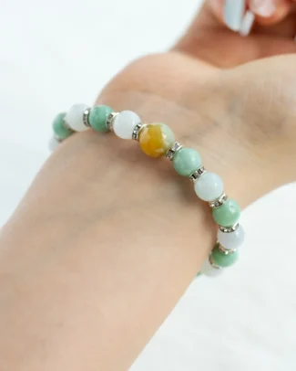 A hand wearing the Multicolor Jadeite Beaded Bracelet—featuring spherical jadeite beads in green and white, accented with a single orange bead and separated by small silver spacers—against a light background.