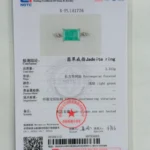 A jewelry certificate featuring a jadeite ring with a rectangular green stone set in silver, details in Chinese and English, official stamps, and a photo of the ring at the top center of the document.