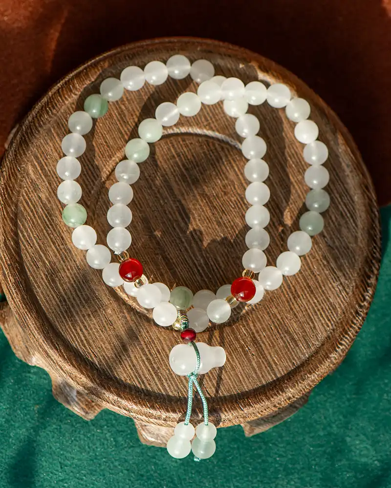 A beaded necklace with white and green beads, accented by a few red beads, is arranged in a circle on a round wooden surface with a green and brown background.