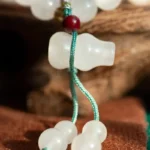 Close-up of white frosted beads and a bottle-shaped bead, strung together with teal cord, against a blurred background of brown fabric and wood.