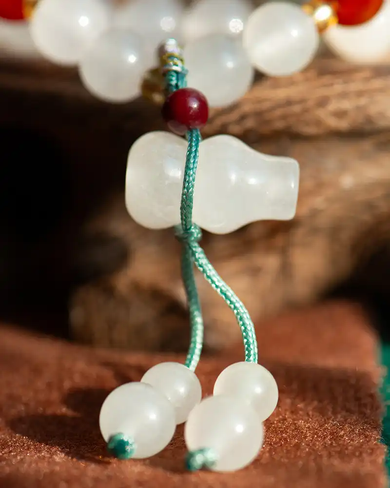 Close-up of white frosted beads and a bottle-shaped bead, strung together with teal cord, against a blurred background of brown fabric and wood.