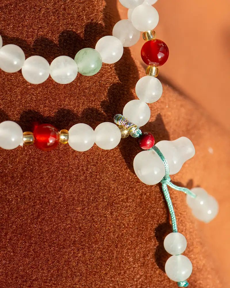 Close-up of a beaded necklace with white, red, and green beads, gold accents, and a turquoise string, displayed against a textured brown background.