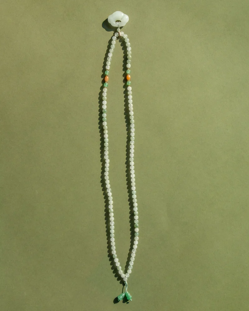 A White and Light Green Quartzite Jade Necklace featuring a donut pendant and green drop accents is displayed against a plain olive green background.