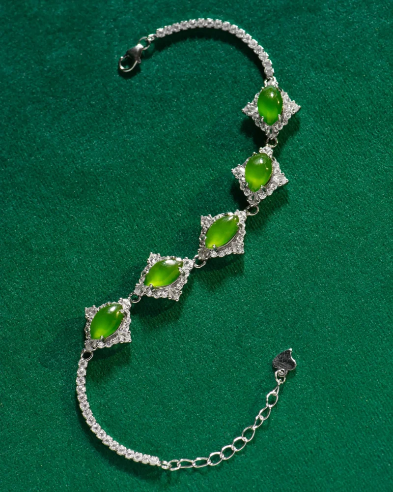 The Green Nephrite Jade Bracelet — Marquise Cabochon Link Line showcases five green marquise cabochon stones set in diamond-shaped frames, elegantly displayed on a green textured surface.