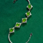 A silver bracelet with four green oval gemstones set in diamond-studded frames, displayed on a green textured background.