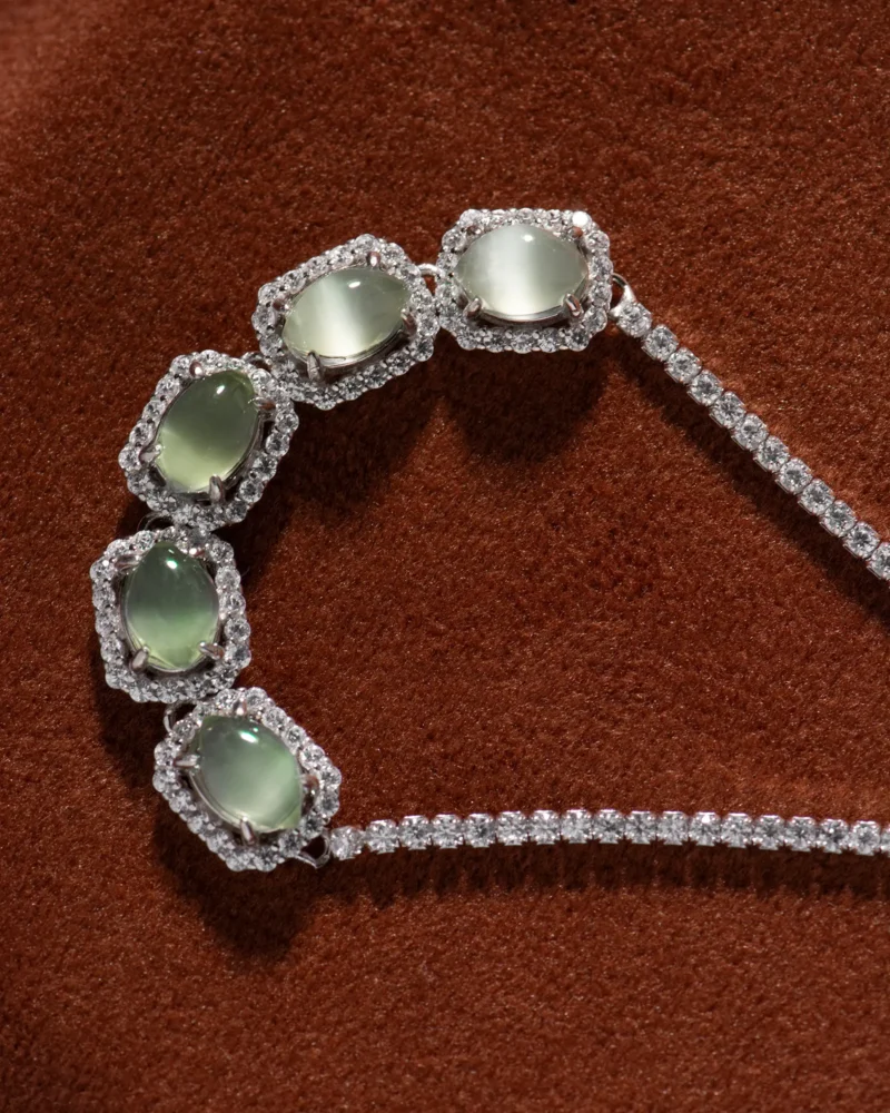 A Grayish-White Nephrite Jade Bracelet featuring marquise cabochon links is displayed on a textured brown surface.