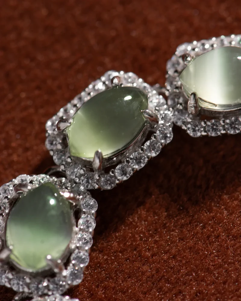 Close-up of a Grayish-White Nephrite Jade Bracelet — Marquise Cabochon Links, showcasing three marquise cabochon grayish-white jade gemstones set in silver and accented with small clear crystals, displayed on a brown textured surface.